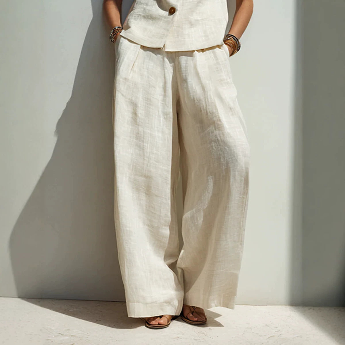 Woman wearing a white linen-blend buttoned vest with wide leg pants.