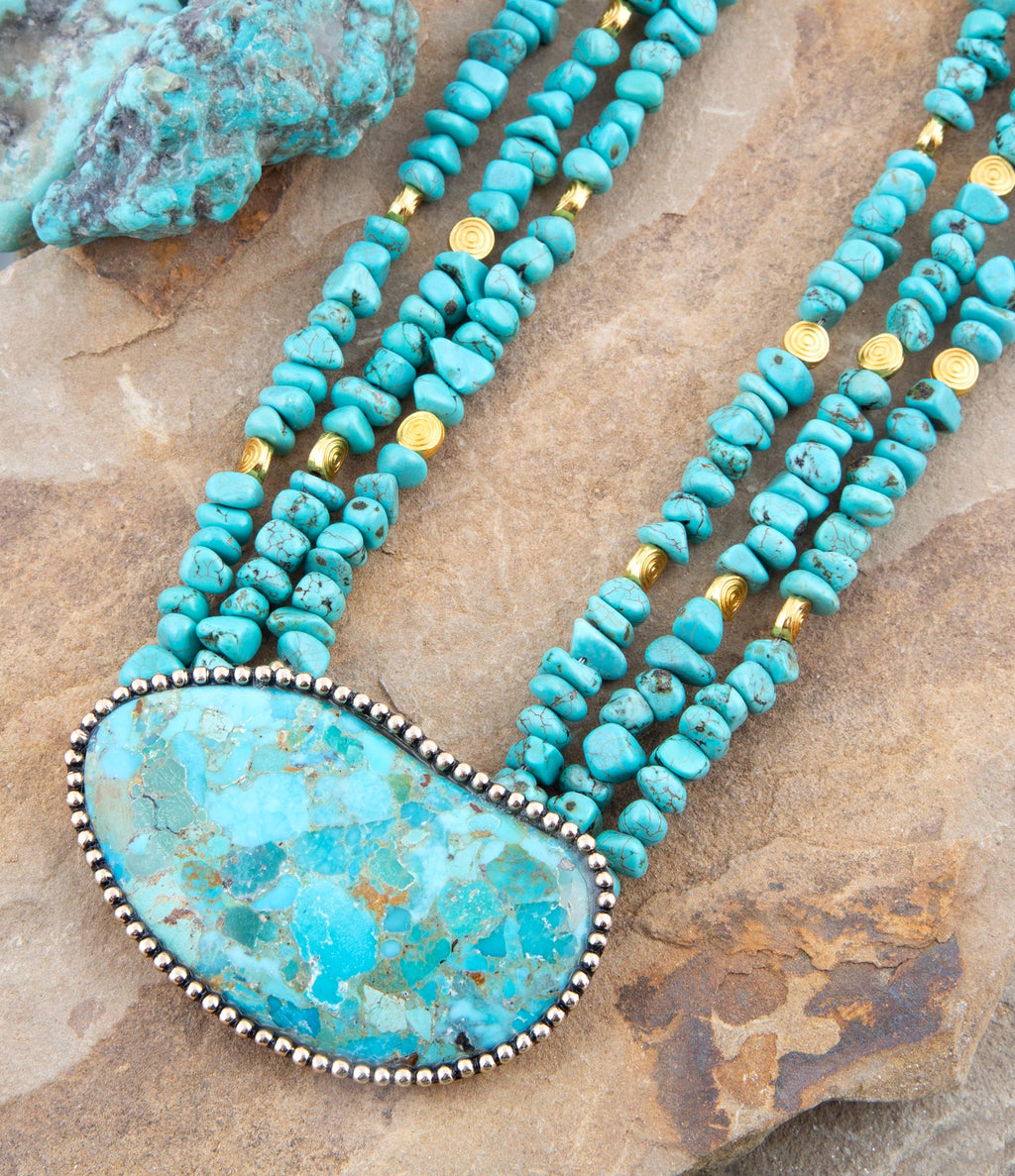 Turquoise beaded statement necklace with large turquoise stone pendant and gold accents.